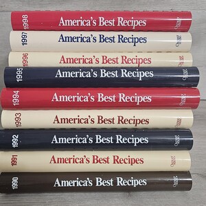 May include: A stack of ten hardcover cookbooks titled America's Best Recipes, published by Oxmoor House. The spines are colored red, cream, navy blue, and brown, each printed with the year from 1990 to 1998, arranged in a vertical column.