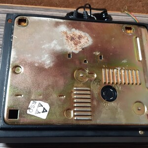 May include: The back of a black rotary phone with a gold-colored metal plate. The plate has a series of small holes and a sticker that says "RSA".