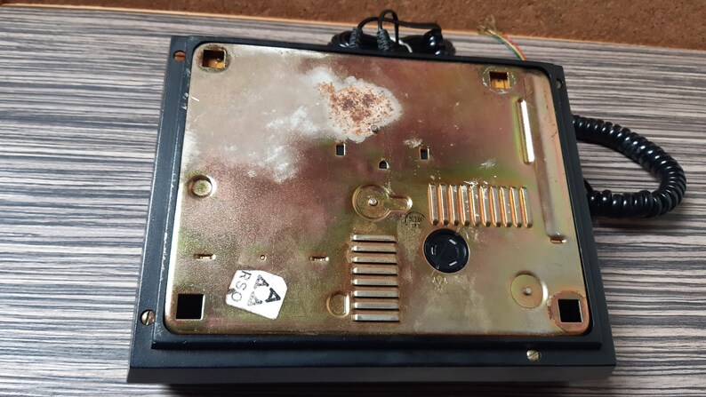 May include: The back of a black rotary phone with a gold-colored metal plate. The plate has a series of small holes and a sticker that says "RSA".
