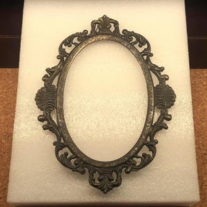 May include: An ornate oval-shaped picture frame with a gold finish and intricate details. The frame is made of metal and has a classic design.