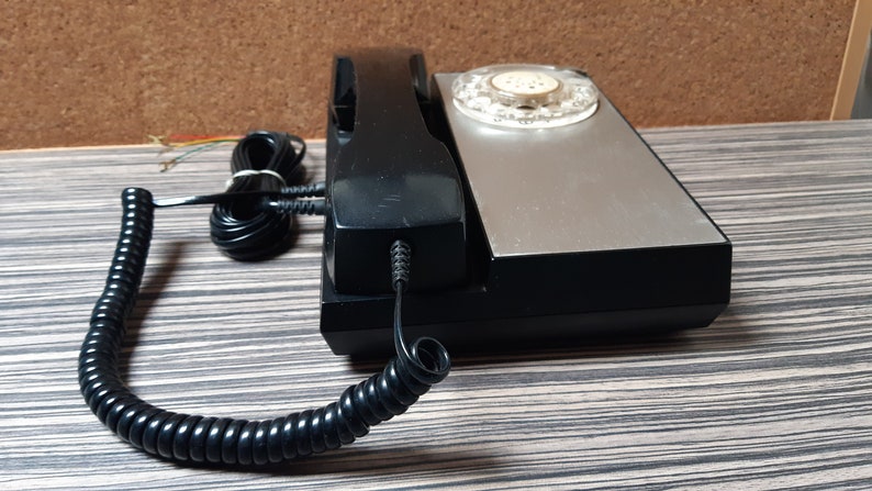 May include: A black rotary phone with a silver faceplate and a coiled black cord. The phone has a black handset and a push-button dial.
