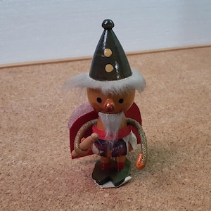 Könnte beinhalten: Eine Holzfigur eines Zwergs, der einen schwarzen Hut mit gelben Punkten, ein rot-weiß gemustertes Hemd und einen weißen Bart trägt. Der Zwerg hält einen Holzstab in der Hand.