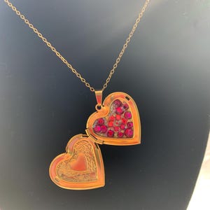May include: A gold heart-shaped locket necklace with a red rhinestone design. The locket is open, revealing a gold interior.