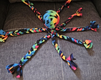 Puede incluir: Un colorido juguete para perros con forma de pulpo. El juguete presenta una bola central con un diseño tie-dye y seis tentáculos trenzados en varios colores, incluyendo azul, verde, amarillo y rojo. Los extremos de los tentáculos están anudados.
