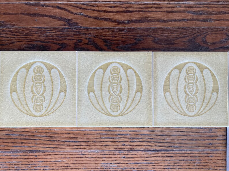 May include: Three cream-colored ceramic tiles with a raised design of a stylized flower with a circle around it. The design is in a light yellow color.