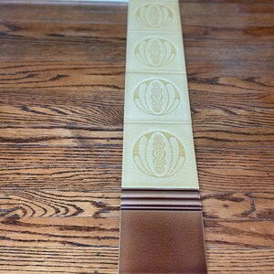 May include: A decorative tile border with a repeating pattern of stylized flowers in a light yellow color. The border is set against a dark brown wood floor.