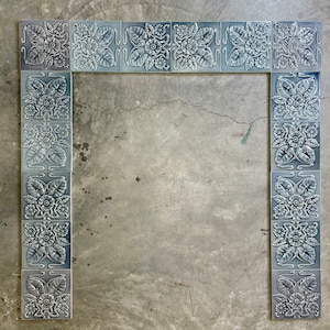 May include: A decorative tile border with a floral design in shades of gray. The tiles are arranged in a rectangular frame, creating a border for a fireplace or other architectural feature.