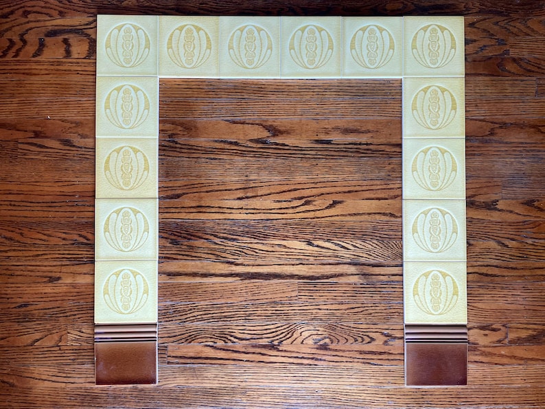 May include: A fireplace surround made of yellow tiles with a brown border. The tiles have a repeating pattern of a stylized flower.