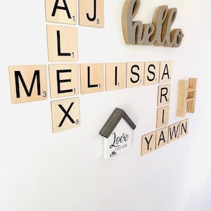 May include: A white wall with a wooden sign that says "Love Lives Here" and a wooden sign that says "hello". There are also several wooden tiles with letters on them, spelling out the names "Alex" and "Melissa".