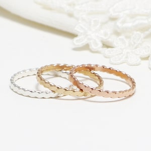 Puede incluir: Tres anillos finos y trenzados en plata, oro y oro rosa. Los anillos están apilados uno encima del otro.