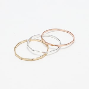 May include: Three thin gold, silver, and rose gold rings with a textured, hammered finish.