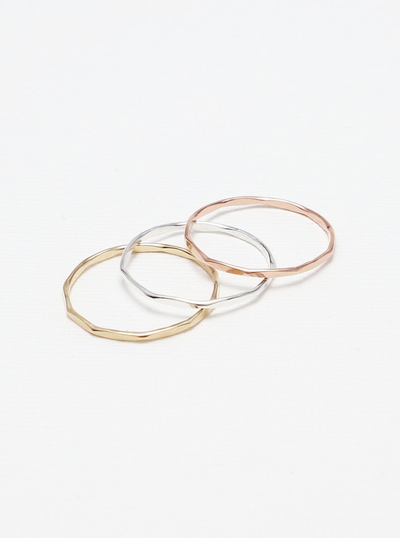 May include: Three thin gold, silver, and rose gold rings with a textured, hammered finish.
