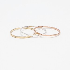 May include: Three thin, hammered metal rings in gold, silver, and rose gold.