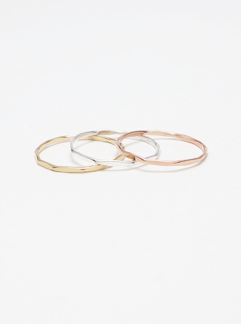 May include: Three thin, hammered metal rings in gold, silver, and rose gold.