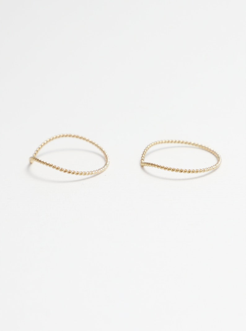May include: Two thin gold rings with a twisted design. The rings are simple and delicate.