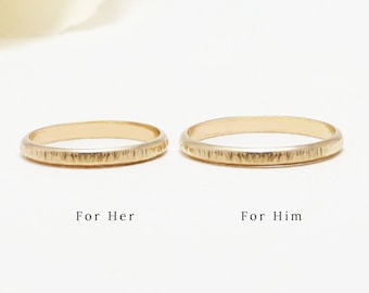 May include: Two gold wedding bands with a textured finish. The bands are side by side, with the larger band on the right and the smaller band on the left.