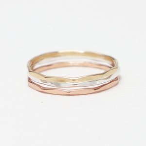 May include: Three thin gold, silver, and rose gold rings stacked together. The rings are all hammered and have a wavy texture.