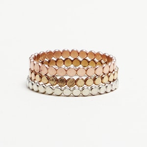 May include: Set of three stacking rings with a hammered finish. The rings are made of silver, gold, and rose gold.