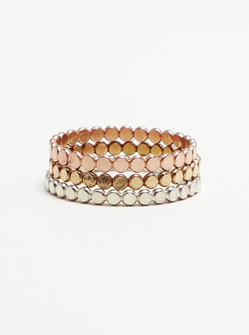 May include: Set of three stacking rings with a hammered finish. The rings are made of silver, gold, and rose gold.