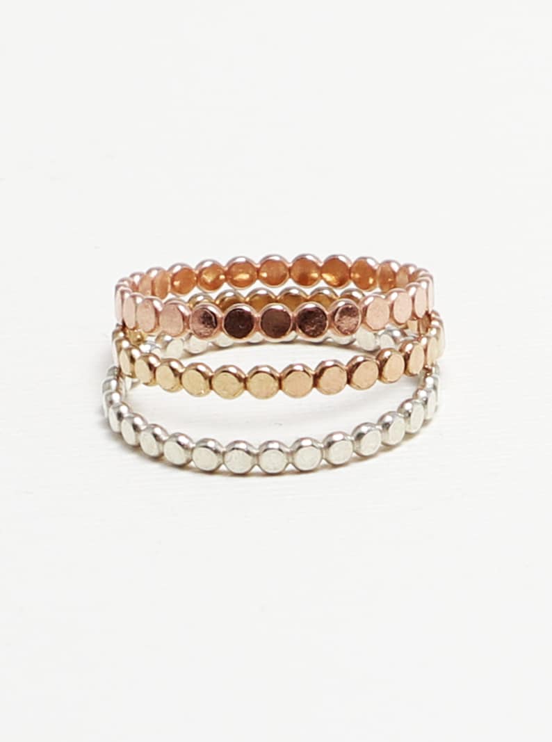 May include: Three delicate stacking rings made of silver, gold, and rose gold. Each ring is composed of small, round beads.