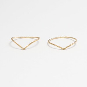 May include: Two gold-toned rings with a twisted design. The rings are shaped like a V.