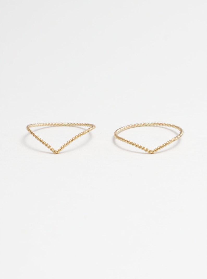 May include: Two gold-toned rings with a twisted design. The rings are shaped like a V.