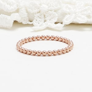 May include: A rose gold beaded ring. The ring is made of small, round beads that are evenly spaced.