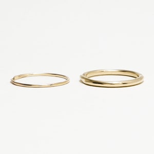 May include: Two gold rings, one thin and one thicker, on a white background.