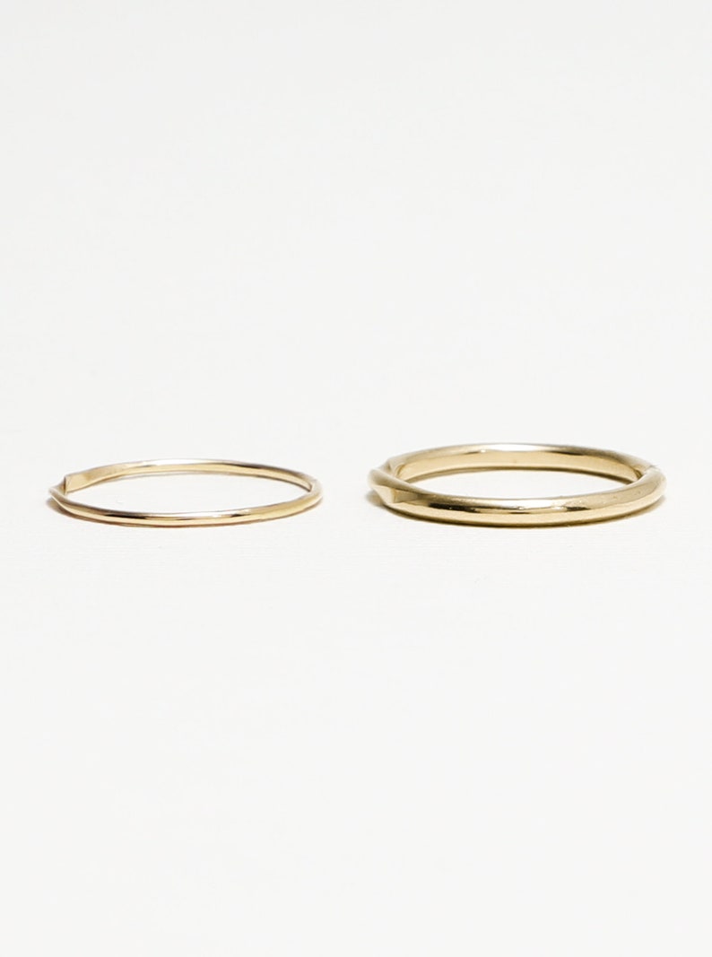 May include: Two gold rings, one thin and one thicker, on a white background.