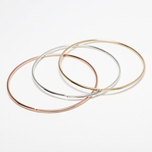 May include: Three simple bangle bracelets in gold, silver, and rose gold.