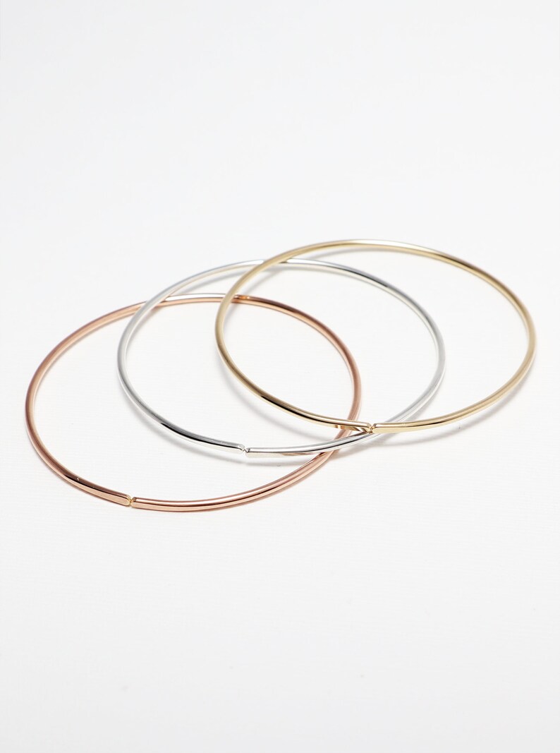 May include: Three simple bangle bracelets in gold, silver, and rose gold.