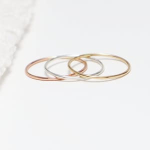May include: Three thin, simple stacking rings in gold, silver, and rose gold.