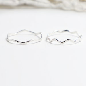 Op de afbeelding: Twee zilveren ringen met een golvend, getextureerd ontwerp. De ringen zijn eenvoudig en delicaat.