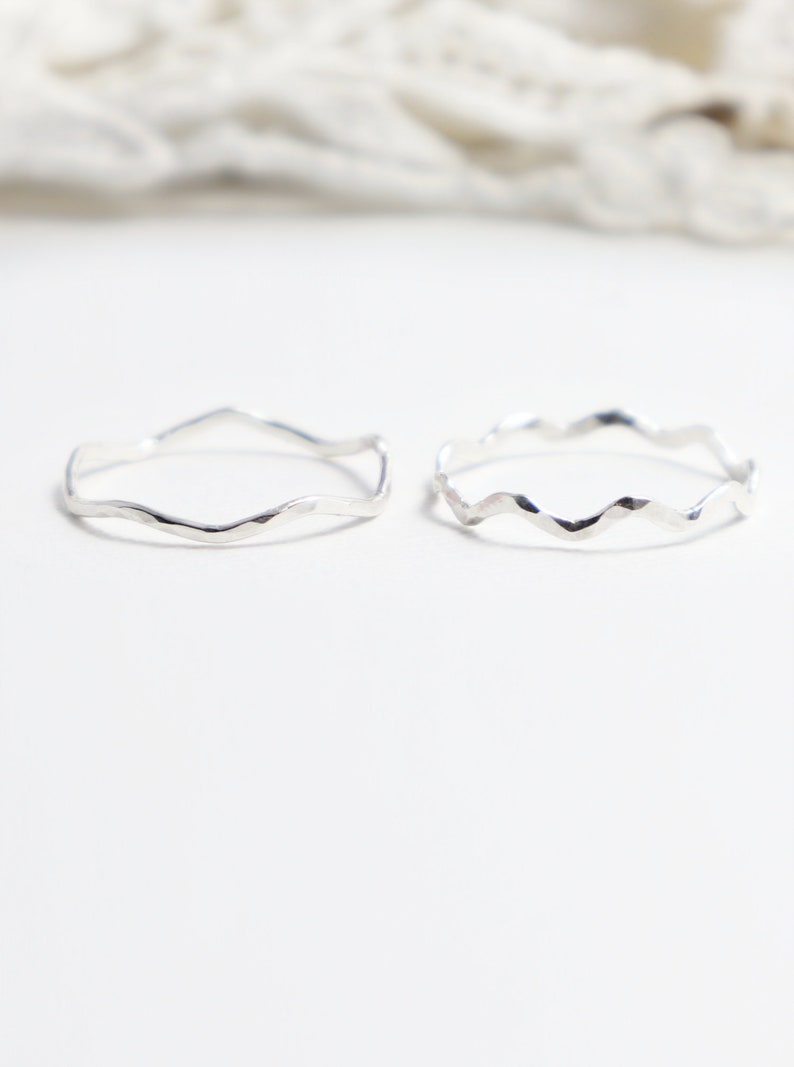 Op de afbeelding: Twee zilveren ringen met een golvend, getextureerd ontwerp. De ringen zijn eenvoudig en delicaat.