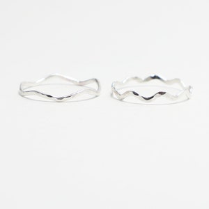 Op de afbeelding: Twee zilveren ringen met een golvend, getextureerd ontwerp. De ringen zijn eenvoudig en delicaat.