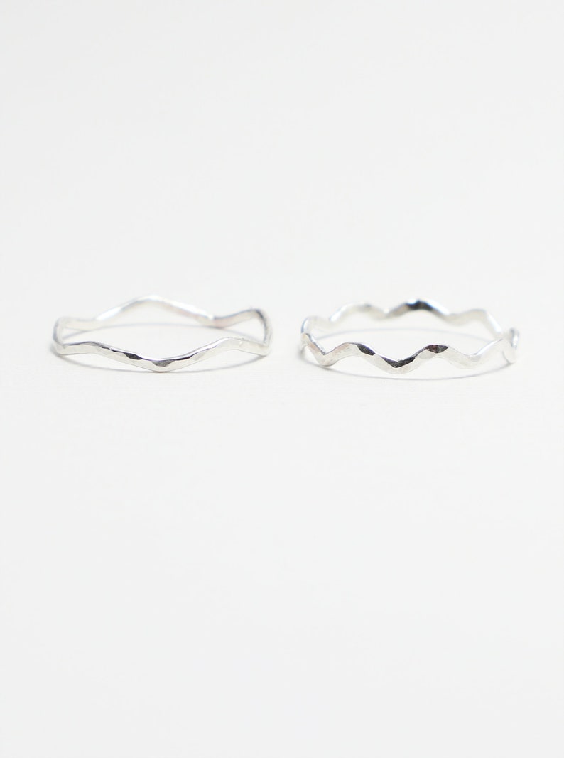 Op de afbeelding: Twee zilveren ringen met een golvend, getextureerd ontwerp. De ringen zijn eenvoudig en delicaat.