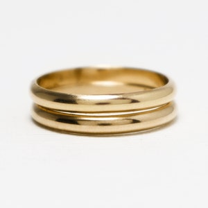 May include: Two gold wedding bands stacked on top of each other. The bands are smooth and shiny.