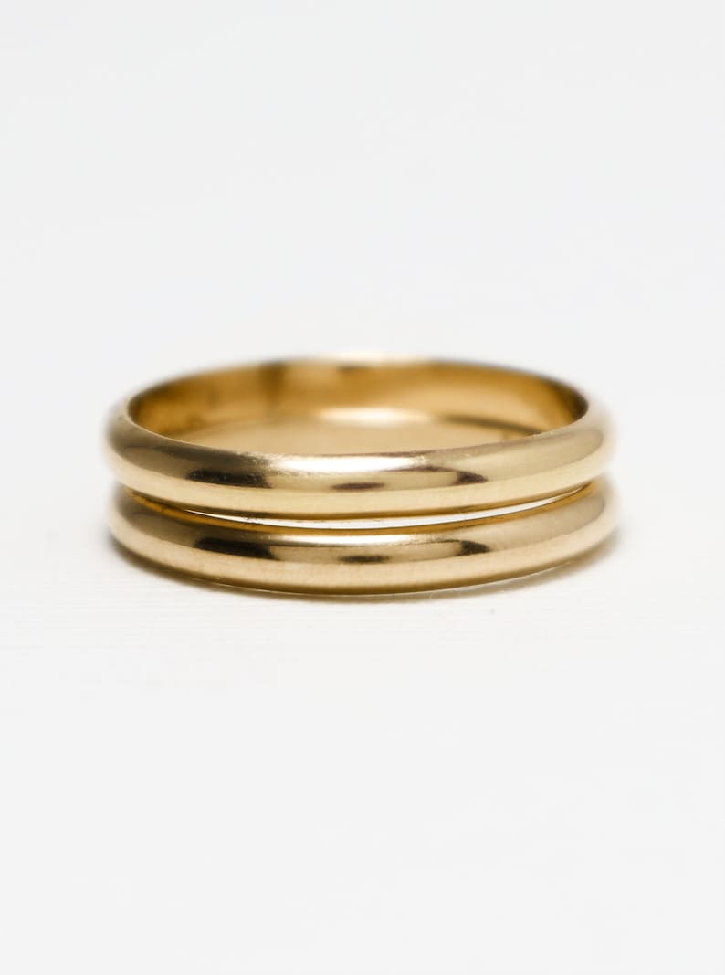 May include: Two gold wedding bands stacked on top of each other. The bands are smooth and shiny.