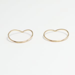 May include: Two gold heart-shaped rings on a white background.