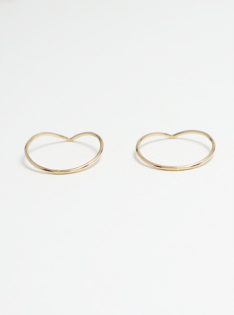 May include: Two gold heart-shaped rings on a white background.