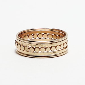 Pu&ograve; includere: Un set di quattro anelli impilabili in oro. Gli anelli sono in metallo sottile e hanno una texture martellata. Un anello ha una fila di piccole perle rotonde.