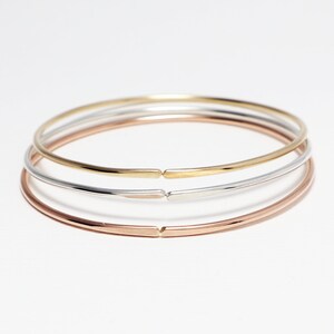 May include: Three simple bangle bracelets in gold, silver, and rose gold.
