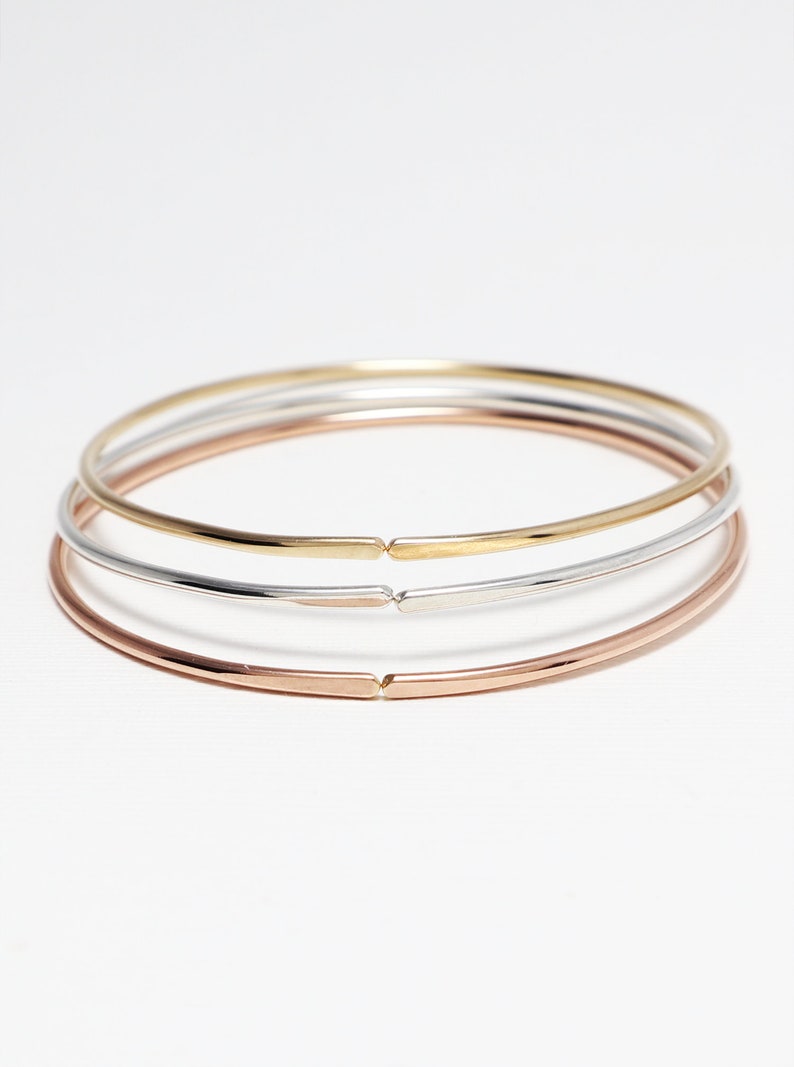 May include: Three simple bangle bracelets in gold, silver, and rose gold.