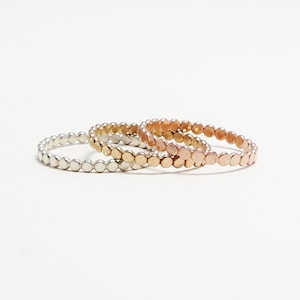 May include: Three stacking rings made of metal. The rings are made of silver, gold, and rose gold. The rings are all the same size and have a beaded design.
