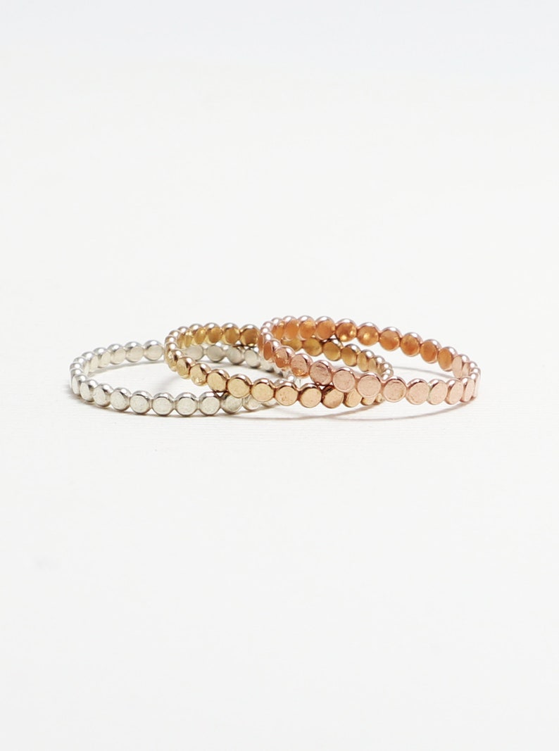 May include: Three stacking rings made of metal. The rings are made of silver, gold, and rose gold. The rings are all the same size and have a beaded design.