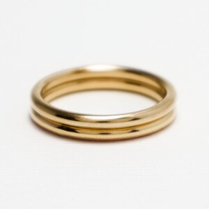 May include: Two gold-coloured rings, possibly metal, are shown against a white backdrop. The rings have a smooth, shiny surface and a simple, classic design. These are likely jewellery items.