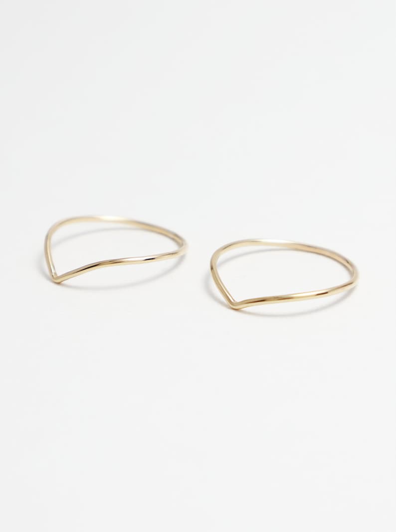 May include: Two gold-coloured, thin, open-ended rings with a V-shaped opening.