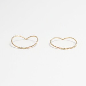 May include: Two gold-toned, twisted wire hoop earrings. The hoops are shaped like a heart.
