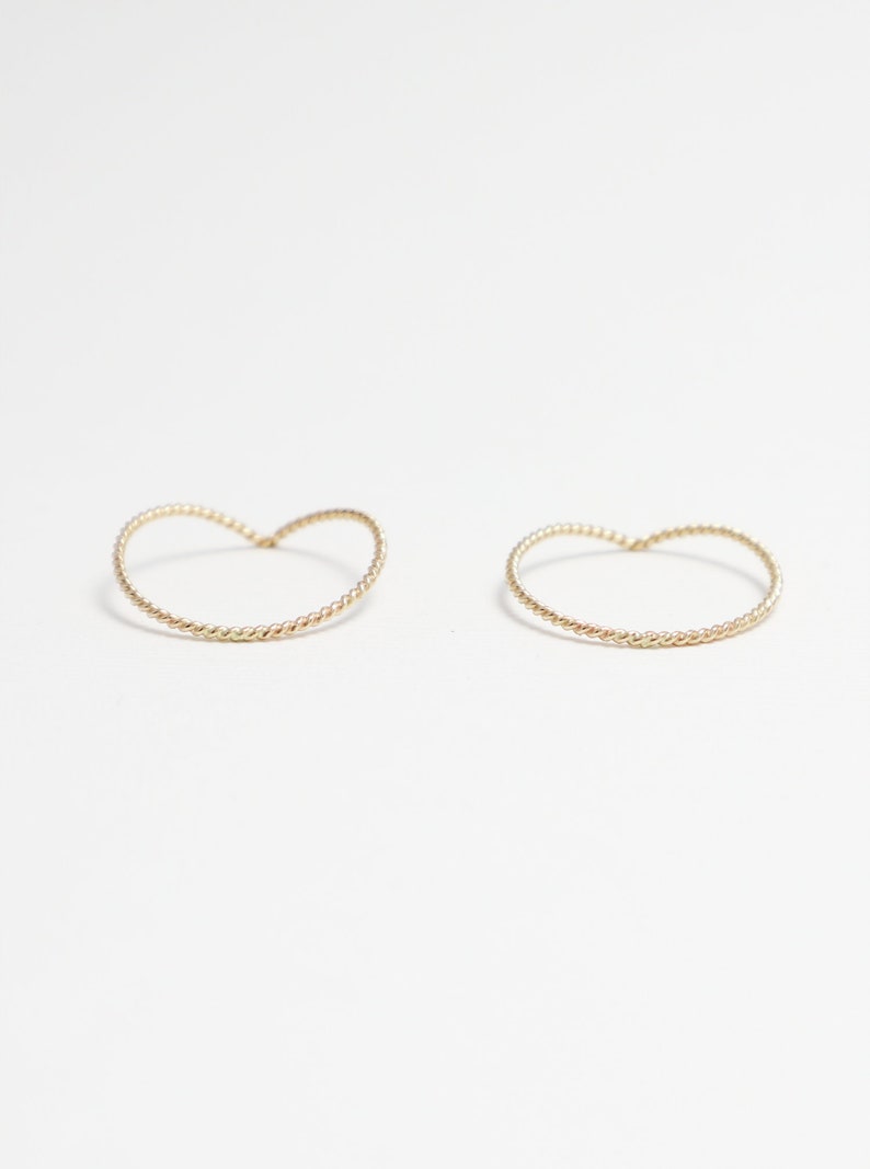 May include: Two gold-toned, twisted wire hoop earrings. The hoops are shaped like a heart.