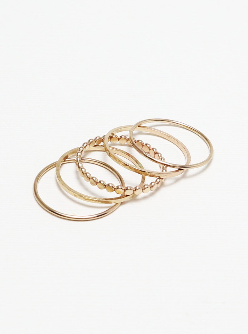 Pu&ograve; includere: Set di cinque anelli in oro, tra cui un anello con design a perline, un anello martellato e tre bande lisce.
